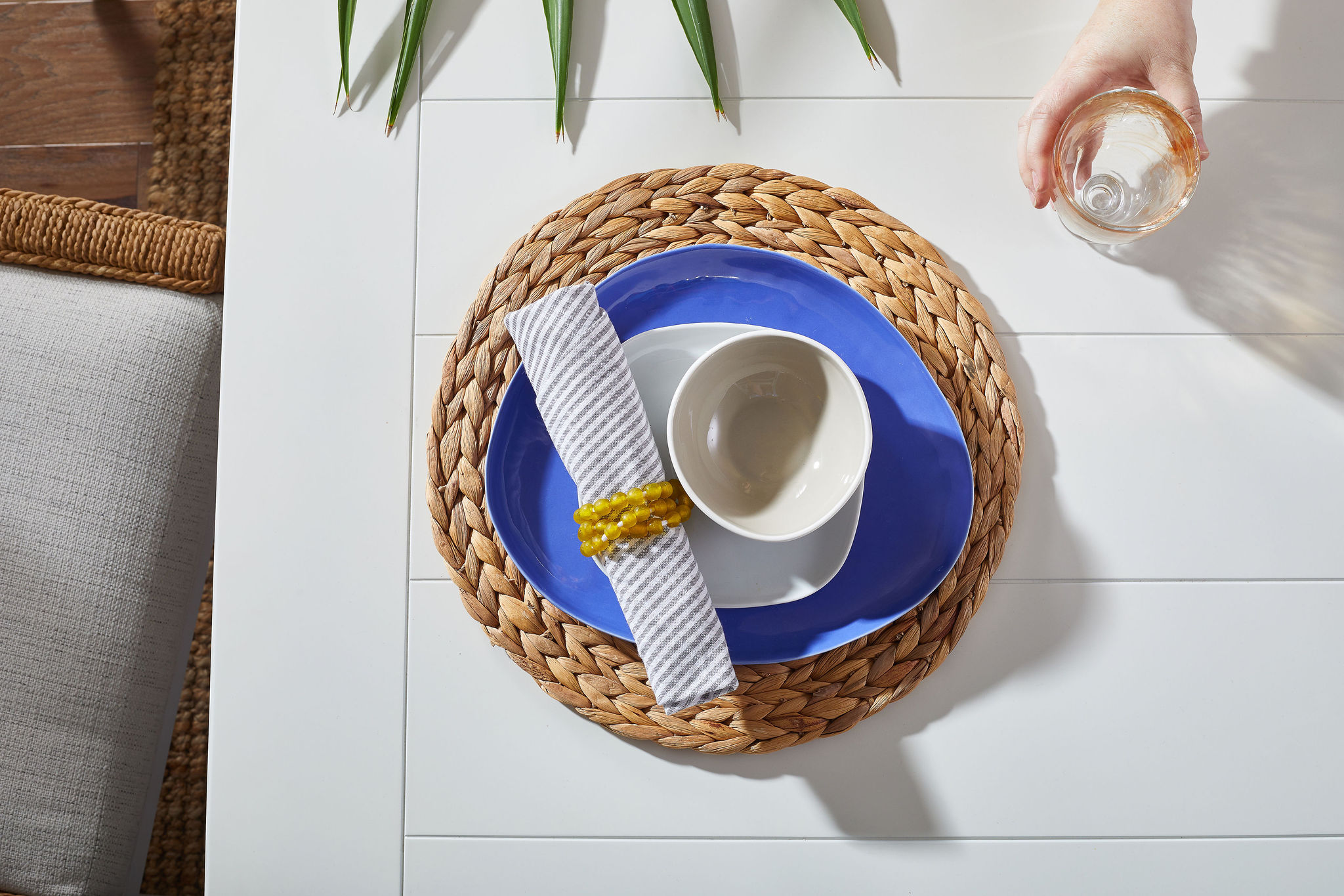 Place setting with a woven placemat, blue base plate, white bowls and a clear glass.