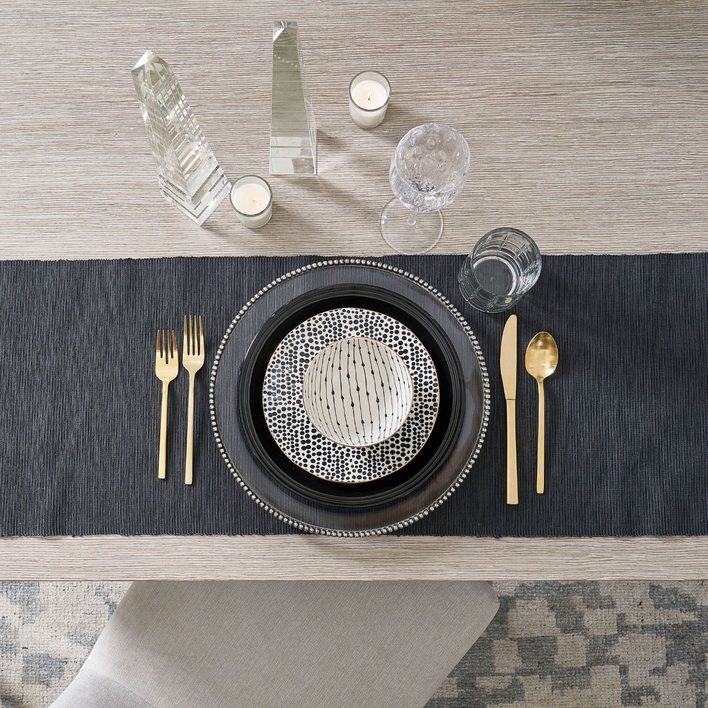 table with black tablecloth, plate, gold flatware, glasses, and patterned bowls